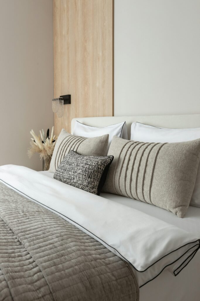 Linge de lit élégant et douillet sur lit avec oreillers beiges et coussin texturé, montrant le confort apporté par le linge de lit.