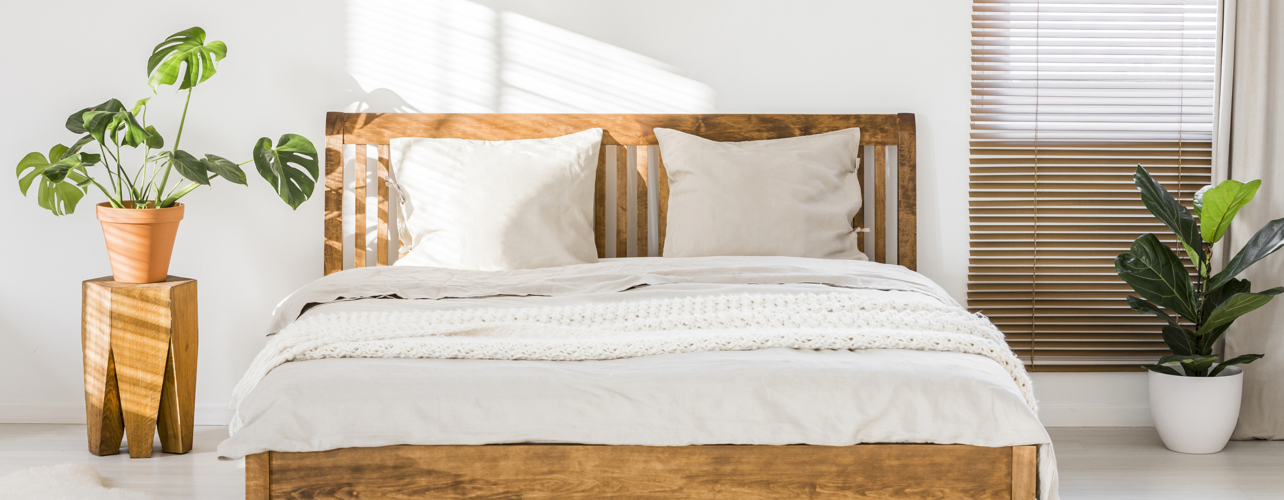 Lit en bois avec linge blanc dans une chambre lumineuse, entouré de plantes.